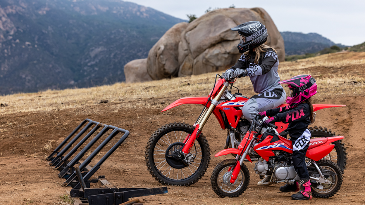 Two riders parked against a rack with their Honda Trail bikes