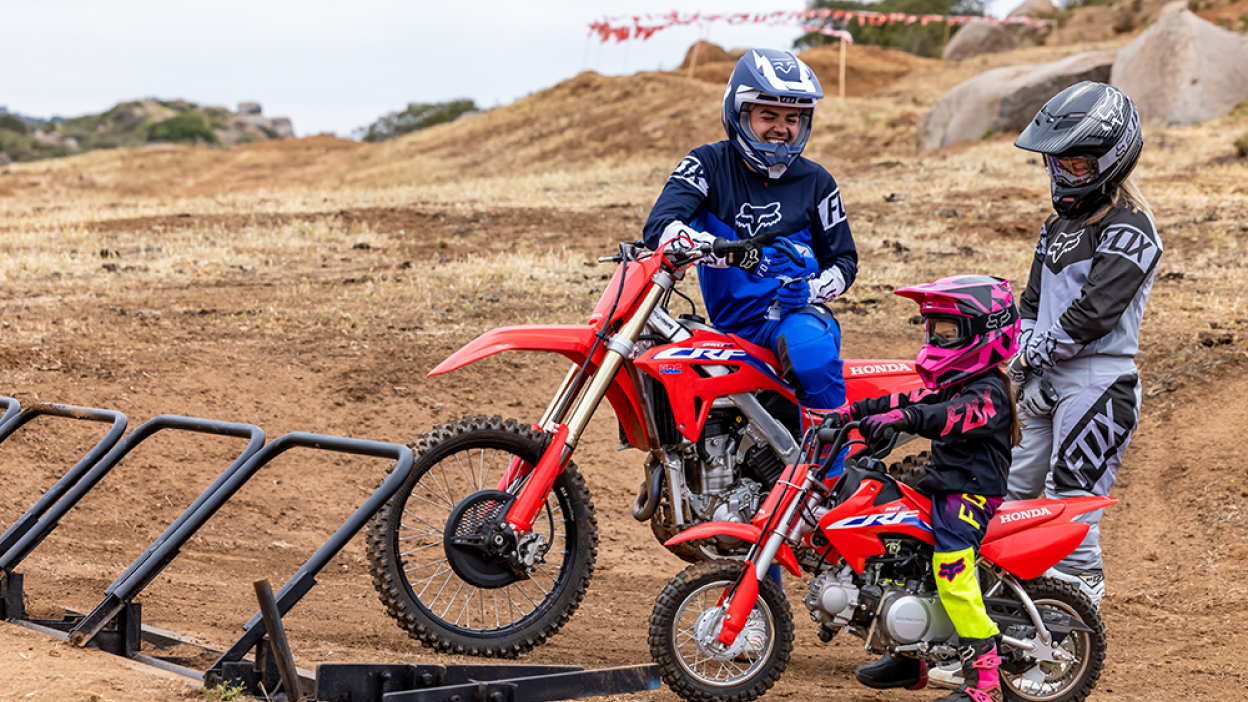 Three riders on Honda Trail dirt bikes parked and having a conversation on a trail