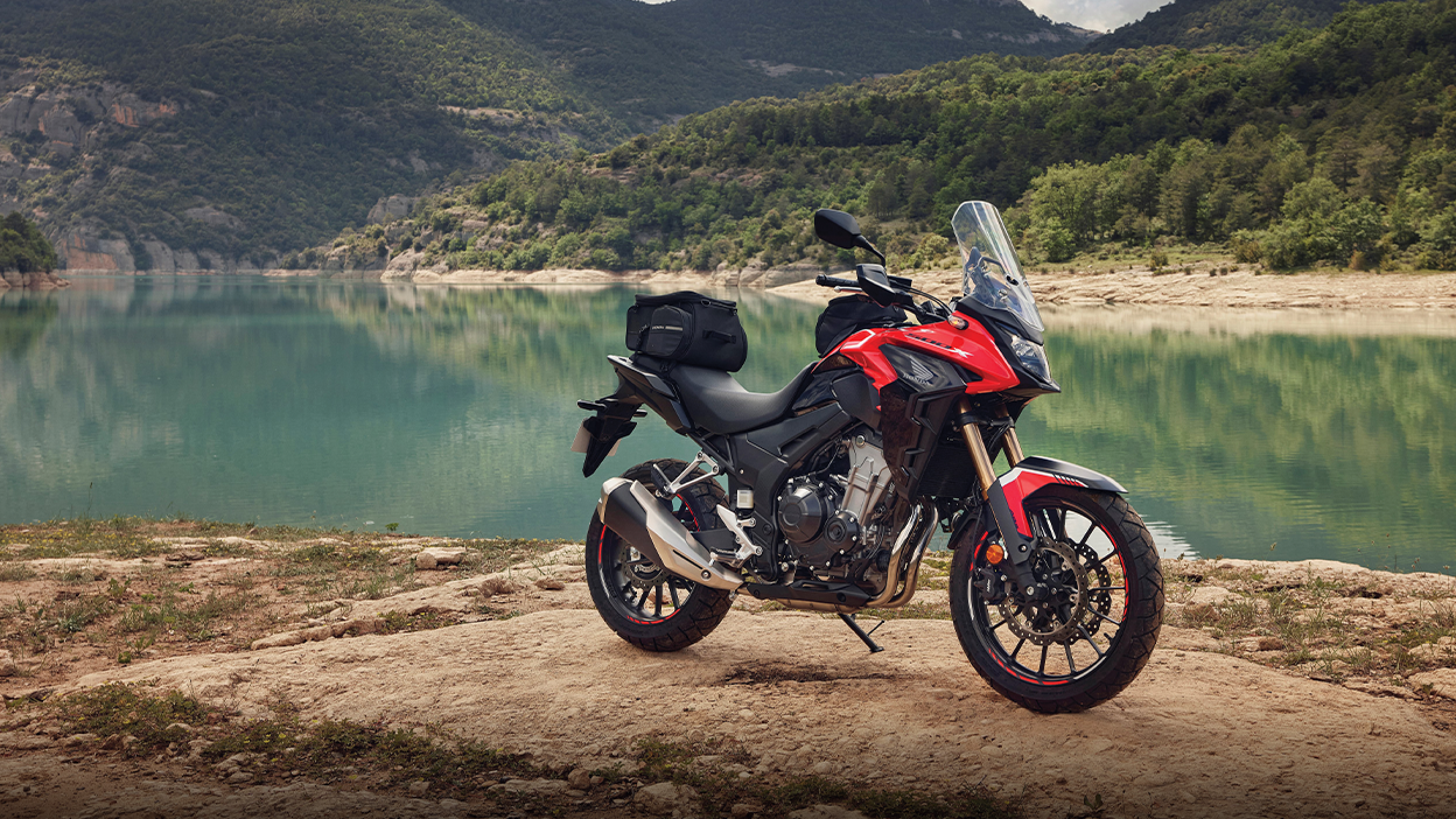 A parked red CB500X beside a blue lake